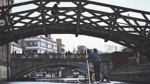 The Mathematical Bridge over the River Cam, with a punt passing underneath and a pedestrian crossing the bridge