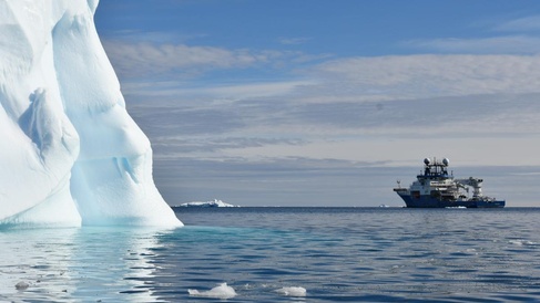 Research vessel at sea in Antarctic waters with iceberg looming large nearby