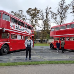 Dr Jack Atkinson standing in front of two old red Routemaster buses at AI conference