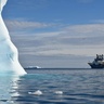 Research vessel at sea in Antarctic waters with iceberg looming large nearby